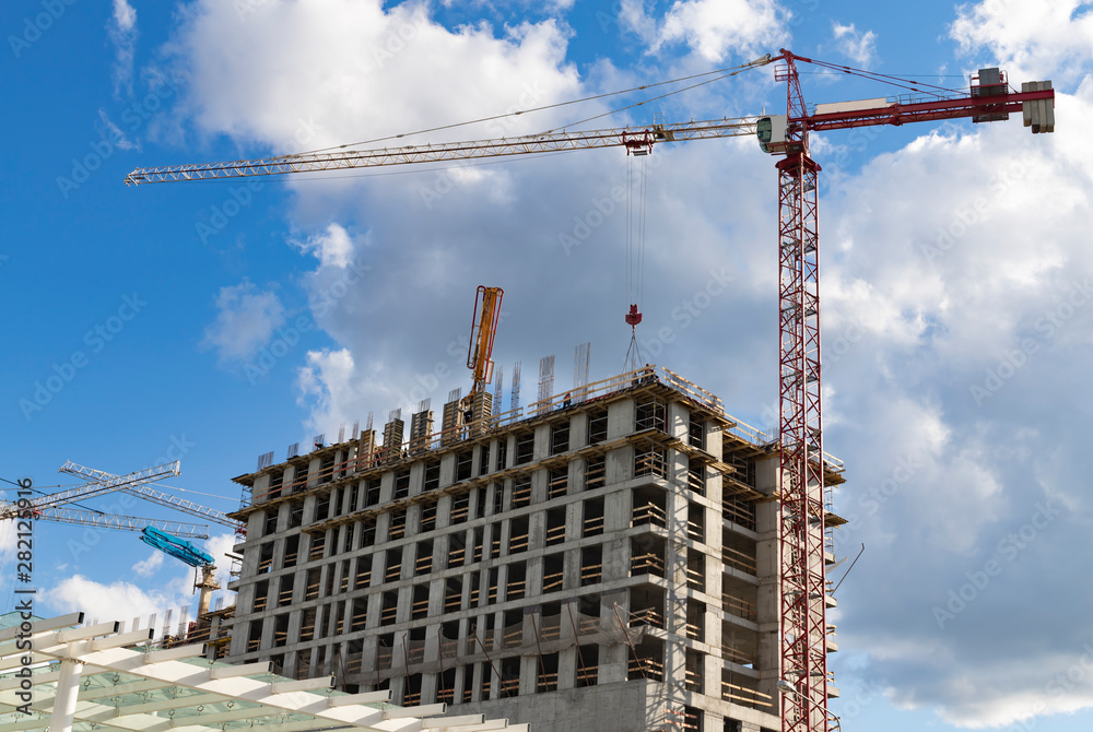 Construction crane and a team of workers are building a multi-storey house against the blue sky with clouds Construction crane and a team of workers are building a multi-storey house against the blue sky with clouds