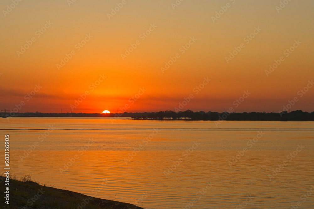 El sol en el horizonte tiñe de amarillo el cielo y el agua del rio 