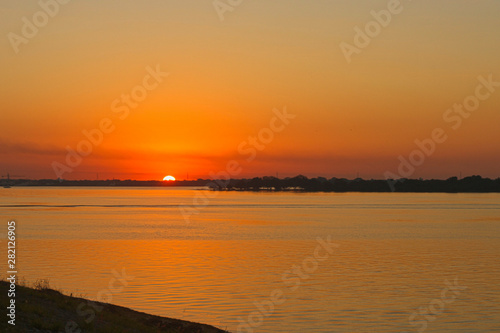 El sol en el horizonte tiñe de amarillo el cielo y el agua del rio 