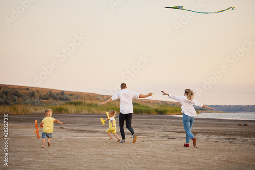 Happy family, father and mother and two children launch a kite on nature at sunset. 