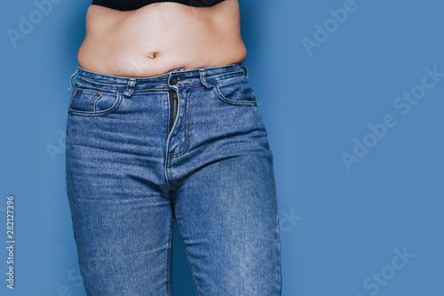 women with belly fat standing in jeans against blue background © Anastassiya 
