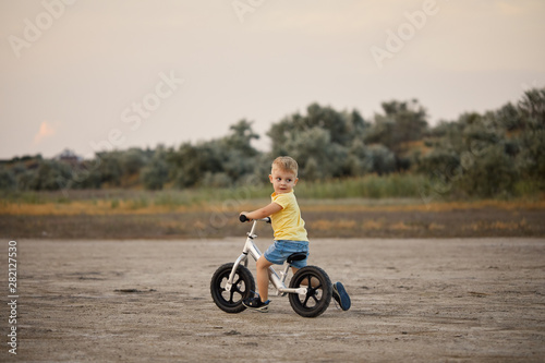 little toddler boy riding balance bike at sunset beach