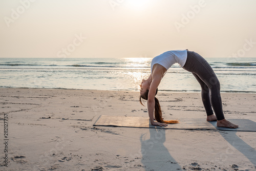 Yoga woman doing yoga pose on the beach at sunrise.