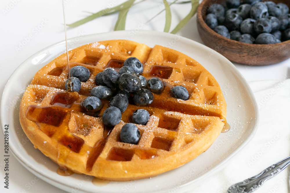Maple Syrup pouring on Belgian waffle with blueberries, Dusted with Powdered Sugar, White Background, Copy Space Maple Syrup pouring on Belgian waffle with blueberries, Dusted with Powdered Sugar, White Background, Copy Space