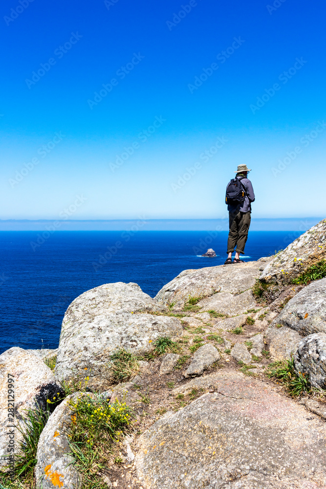 Male pilgrim on the rocks of Cape Finisterre, Cabo Fisterra or Cabo Finisterre - the end of the Way of St. James, Camino de Santiago, Galicia, Spain