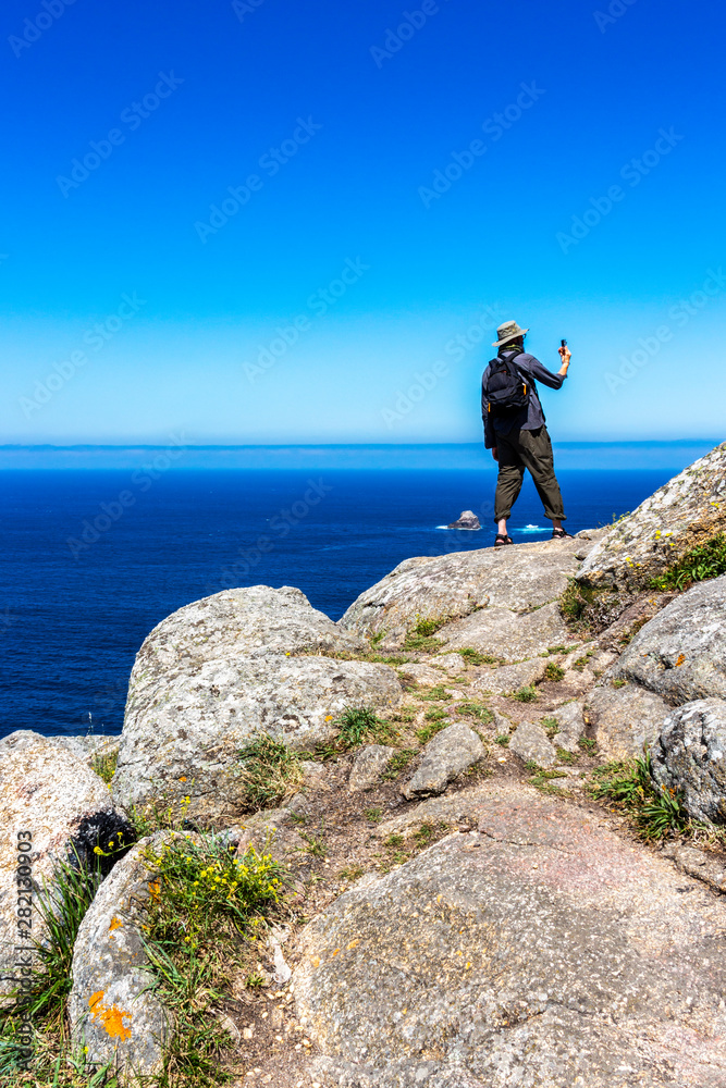 Obraz premium Male pilgrim on the rocks at Cape Finisterre, Cabo Fisterra - the end of the Way of St. James takes pictures with digital compact camera
