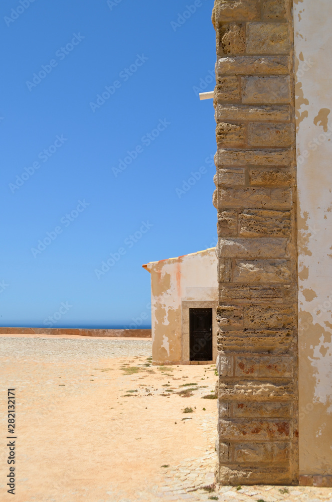 Old White Building with Brick Wall on Bright Blue Sky