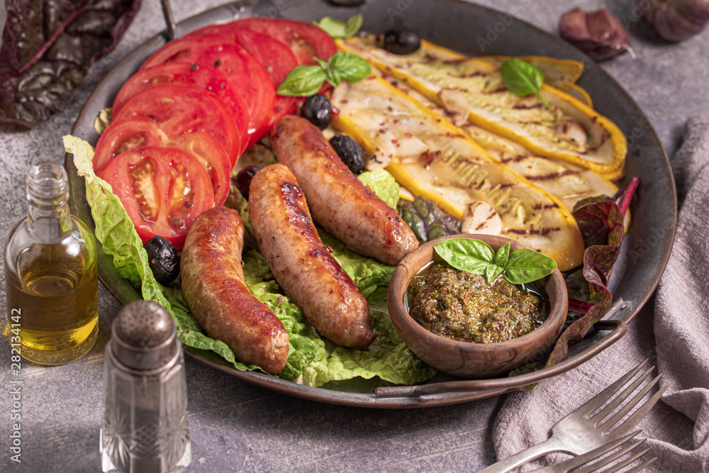 Roasted sausages with grilled courgette and tomatoes on metal tray