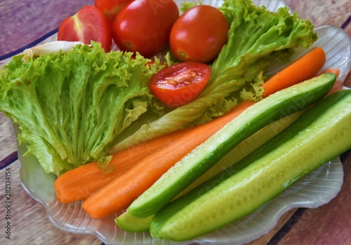 fresh lettuce, tomatoes, cucumbers, carrots and a clove of garlic on a plate of shell