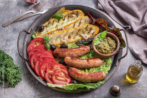 Roasted sausages with grilled zucchini and tomatoes on metal tray