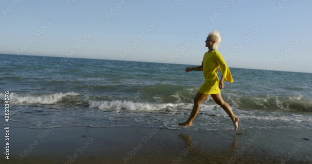happy blonde woman is running over wet sandy shore of ocean in evening time happy blonde woman is running over wet sandy shore of ocean in evening time