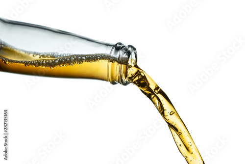 Fotografie Stop action closeup of golden amber beer pouring from clear bottle on white  bac