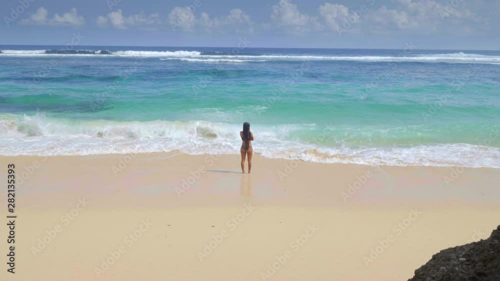 Young tanned woman with dark long hair is standing in water on tropical beach with bright sand in sunny day filmed panoramic in slow motion Young tanned woman with dark long hair is standing in water on tropical beach with bright sand in sunny day filmed panoramic in slow motion