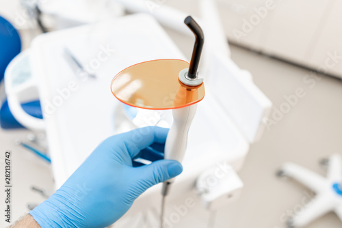 Dental polymerization lamp in dentist hand, with UV light and laser. Stomatological instrument in the dentist clinic. Medicine, health, stomatology concept.