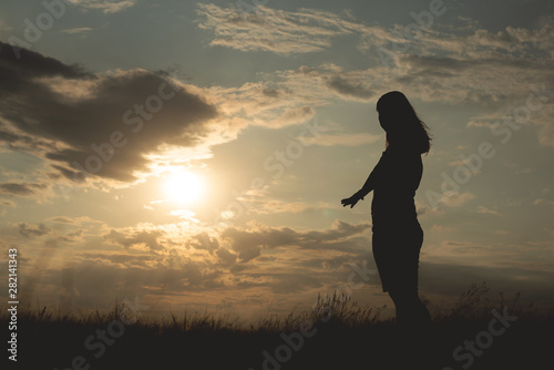 Silhouette of young woman in a sunset rays which is turned around and is stretching her hand to call follow her.