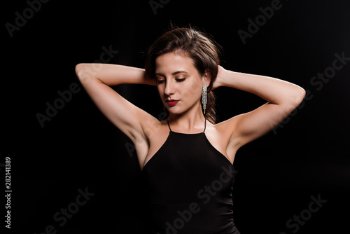 young woman touching hair while standing in dress isolated on black