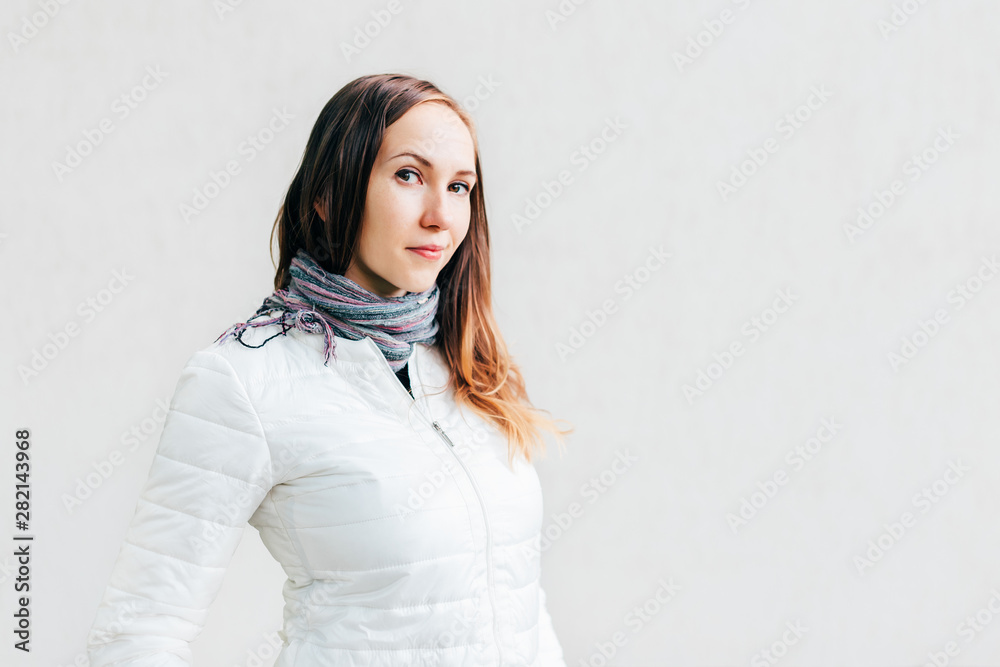 Young Caucasian brunette looks into lens with little smile on background monochrome wall. Young Caucasian brunette looks into lens with little smile on background monochrome wall.