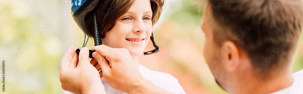 panoramic shot of son smiling and looking at dad while father putting helmet panoramic shot of son smiling and looking at dad while father putting helmet