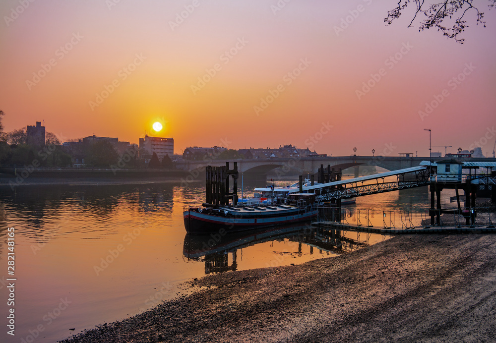 View of romantic scene in Putney bridge area at sunrise, with colorful sky reflected in Thames river in London
