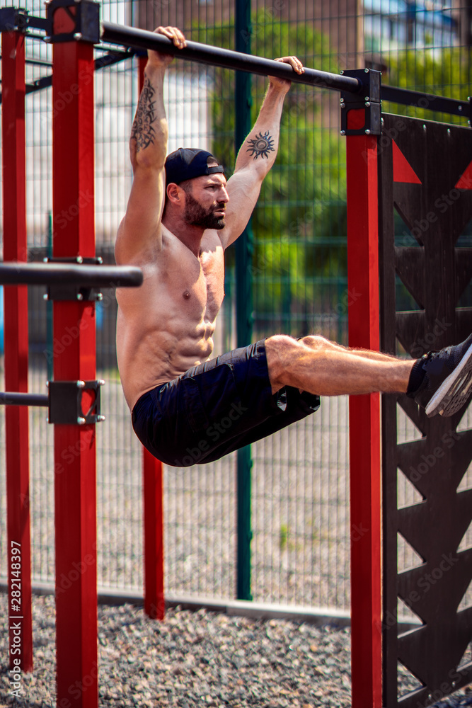 Fototapeta premium Strong Muscular bearded man doing abdominal exercise on horizontal bar at street gym yard. Strength and motivation. Outdoor workout. fitness, sport, exercising, training and lifestyle concept .