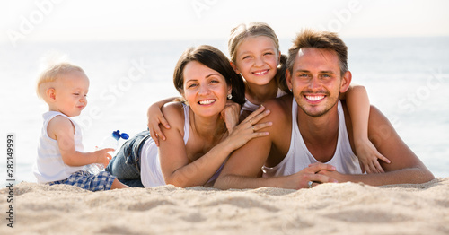 parents with two kids lying on the beach.