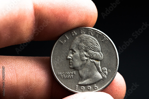 Man's hand holding a silver American coin, close-up of a quarter dollar coin isolated over black. Bag, dollars.