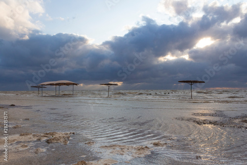 Sea waves flood the beach with beach umbrellas during a storm on the sea on a summer evening at sunset.  © NATALIA