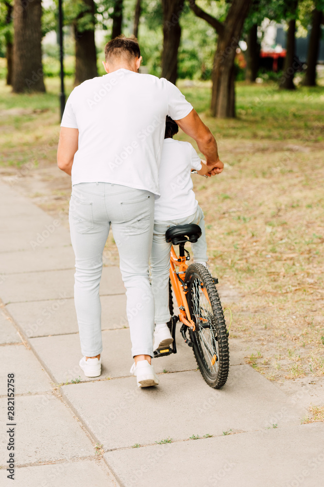 full length view of son riding bicycle while father helping boy
