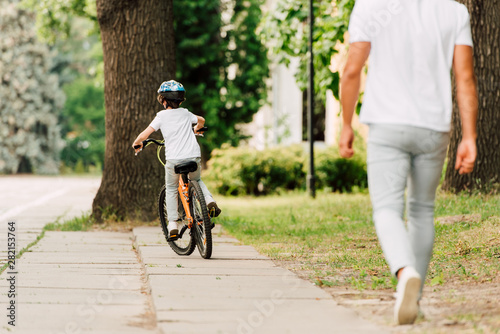 back view of kid riding bicycle while father walking after son