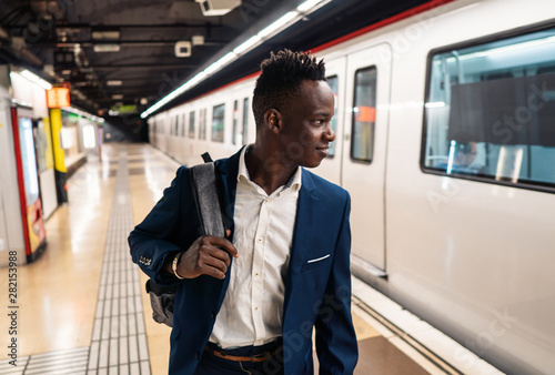 African American businessman wearing blue suit and backpack in metro subway. Business concept
