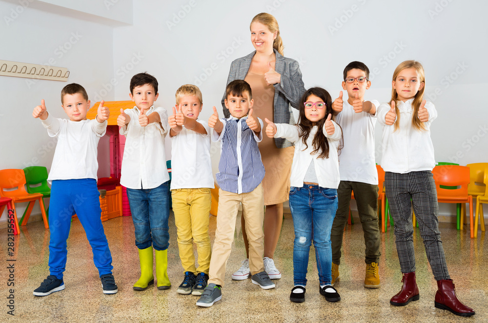 Fototapeta premium Portrait of cheerful female teacher with her happy schoolkids in classrom