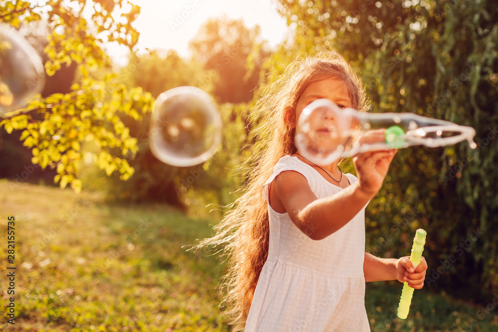 Little cute girl blowing bubbles in summer park. Kid having fun outdoors - obrazy, fototapety, plakaty 