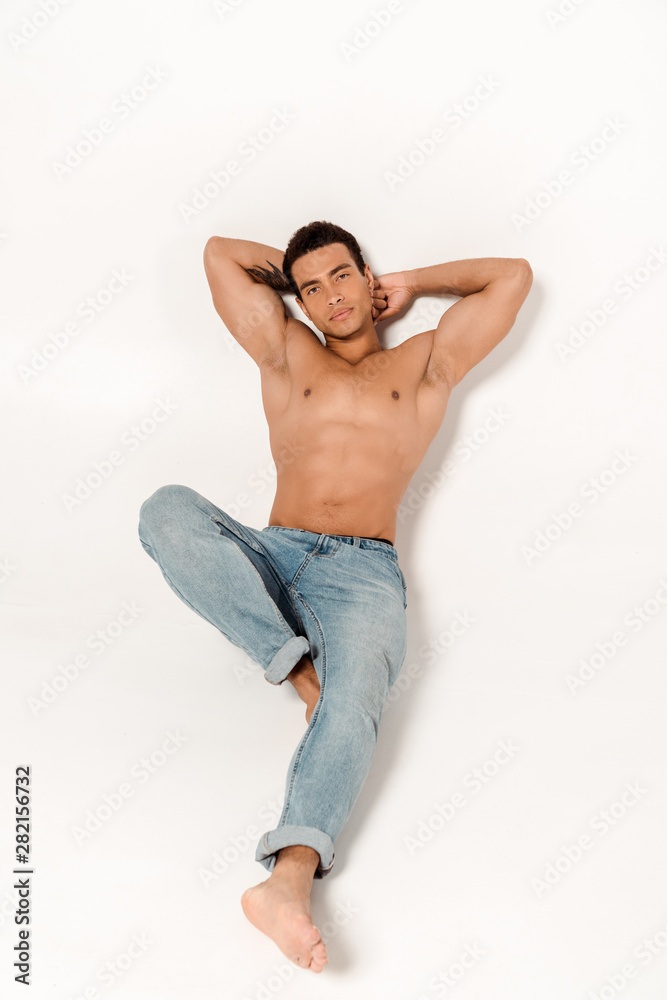 handsome shirtless man in blue jeans lying and looking at camera on white