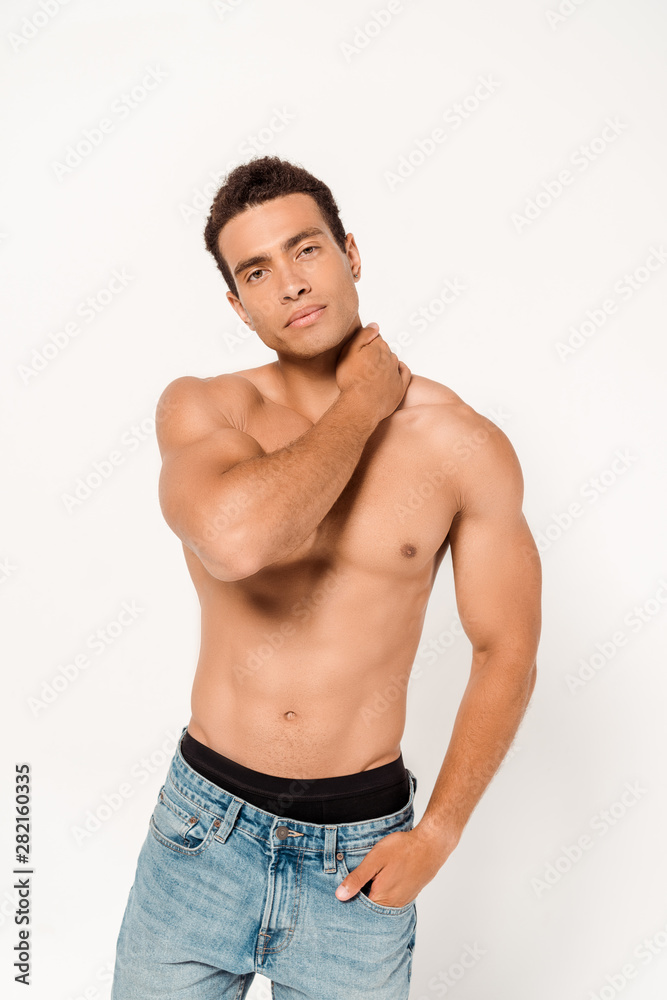 muscular mixed race man standing with hand in pocket and touching neck on white