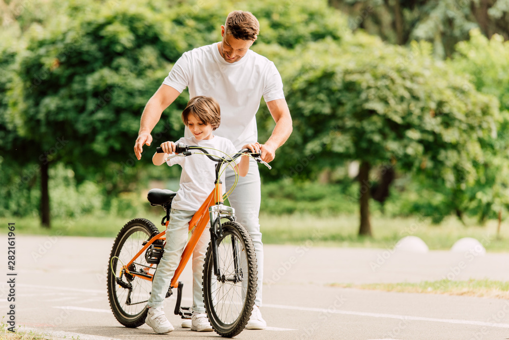 full length view of father and son looking on bicycle while standing on road