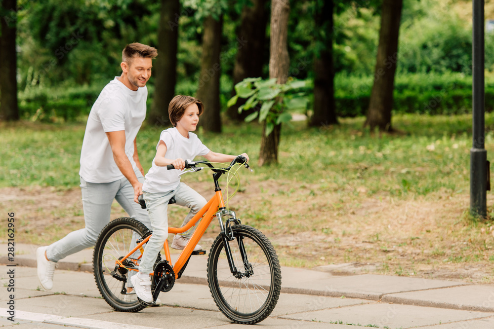 full length view of father pushing sit of bike and running after son while kid riding bicycle full length view of father pushing sit of bike and running after son while kid riding bicycle
