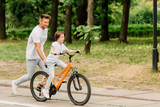 full length view of father pushing sit of bike and running after son while kid riding bicycle