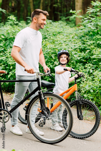 full length view of fahter and son standing with bicycles while boy looking at dad
