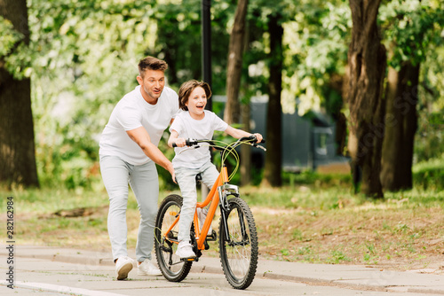 full length view of father pushing bike while son ridding on bicycle