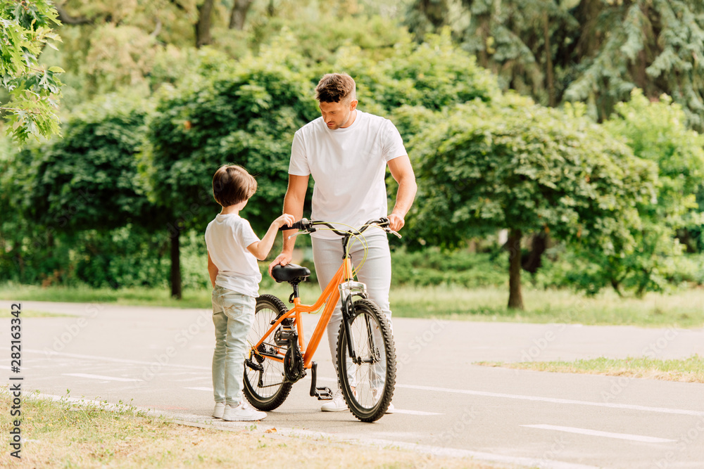 full length view of father checking bicycle while son standing near dad