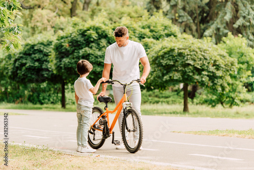 full length view of father checking bicycle while son standing near dad