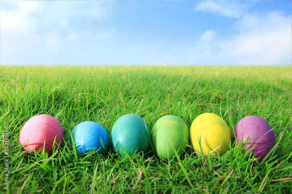 Many Easter eggs, many colors are placed on the green grass, the backdrop is the sky.