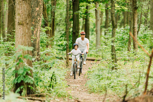 full length view of father and son riding on path in forest