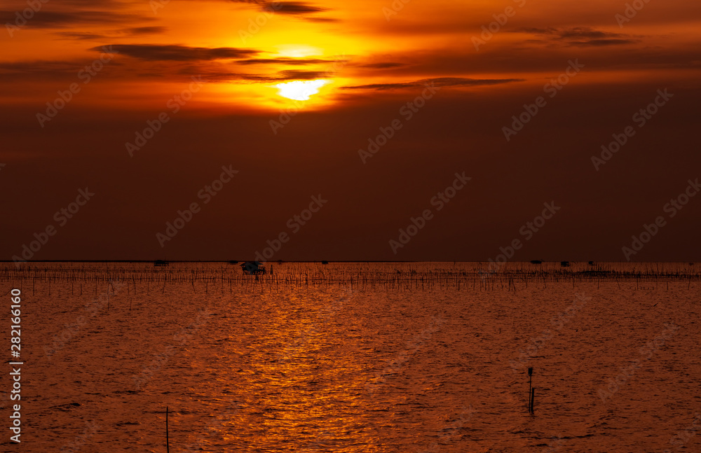 Beautiful sunset over the sea. Dark and golden sunset sky and clouds. Nature background for tranquil and peaceful concept. Sunset at Chonburi, Thailand. Art picture of sky at dusk. Farming in the sea.