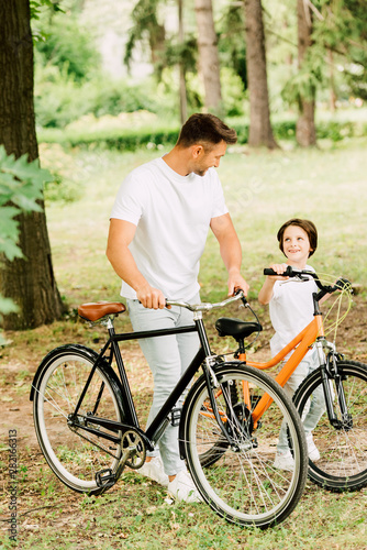 full length view of father and son with bicycles looking at each other