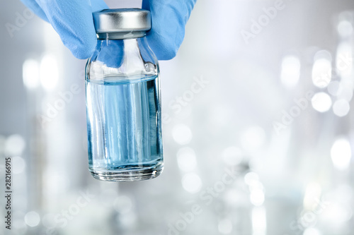 Healthcare concept with a hand in blue medical gloves holding a vaccine vial with blue liquid photo