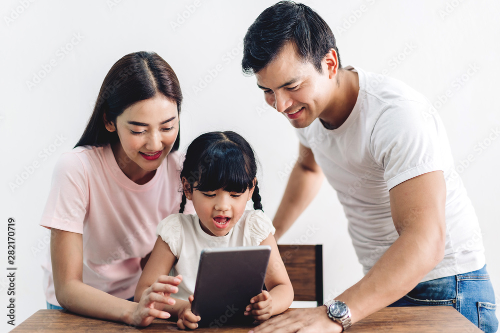 Happy family father and mother with daughter sitting and looking at tablet computer together in the living room at home Happy family father and mother with daughter sitting and looking at tablet computer together in the living room at home