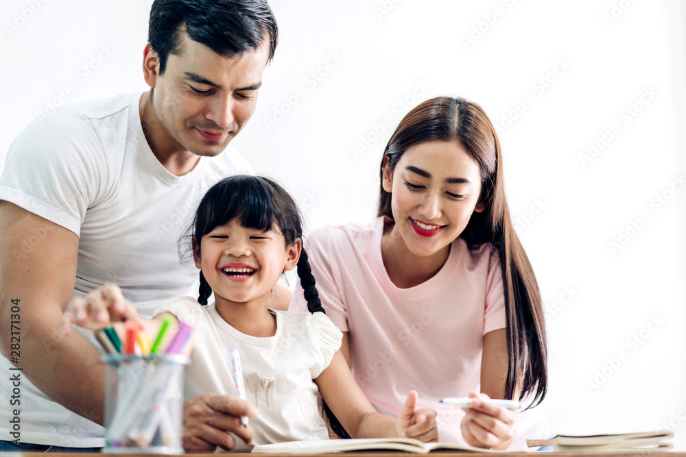 Happy family father and mother with daughter learning and writing in notebook with pencil making homework at home.Education concept Happy family father and mother with daughter learning and writing in notebook with pencil making homework at home.Education concept