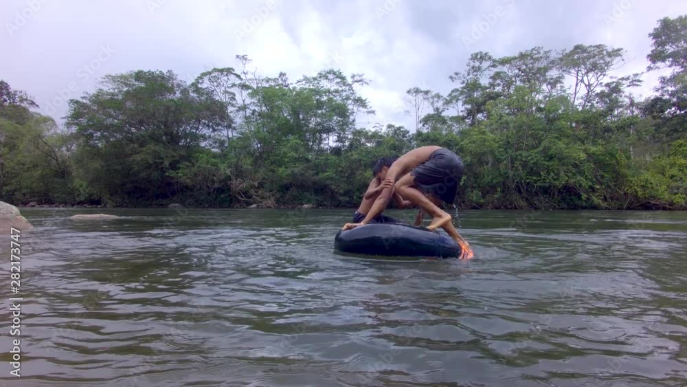 Indigenous Young Boys Playing Trying To Balance Over A River Inner Tube