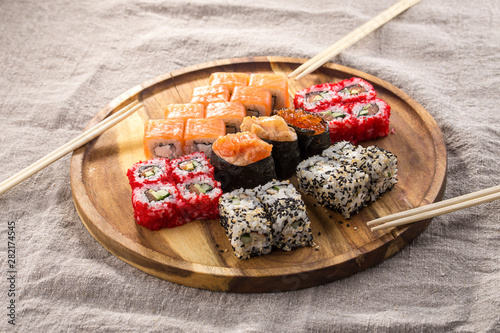 Japanese food restaurant sushi maki roll set on wooden round board with chopsticks on fabric grey background
